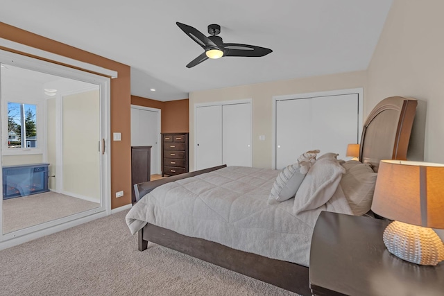 bedroom featuring a ceiling fan, baseboards, a glass covered fireplace, carpet flooring, and two closets