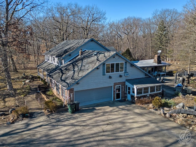 view of front of property featuring aphalt driveway, brick siding, a chimney, and a garage