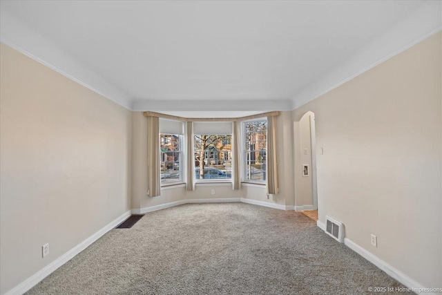 carpeted empty room with arched walkways, visible vents, and baseboards