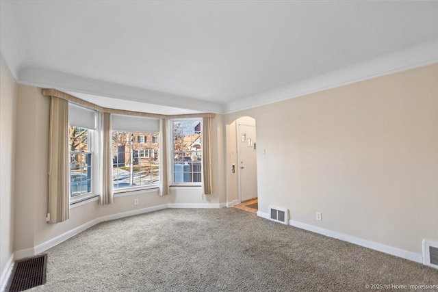 carpeted empty room featuring arched walkways, visible vents, and baseboards