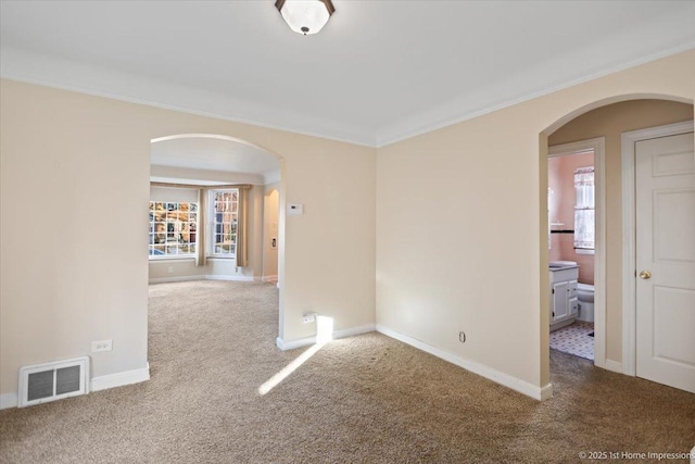 carpeted spare room with arched walkways, plenty of natural light, and visible vents