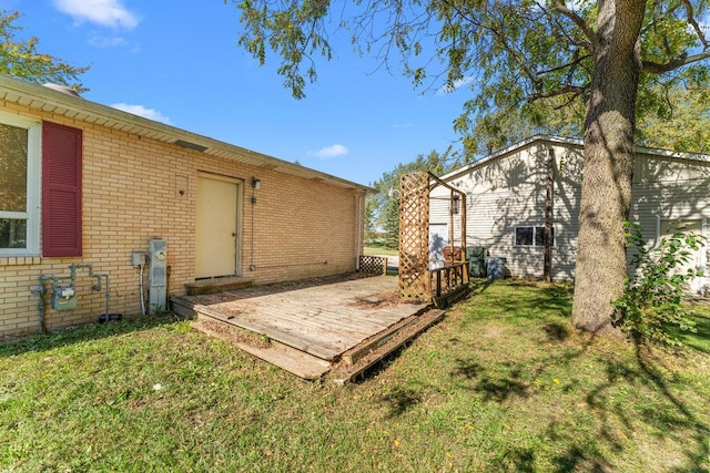 rear view of property with a deck, a lawn, and brick siding