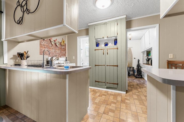 kitchen featuring a peninsula, light countertops, crown molding, a textured ceiling, and a sink