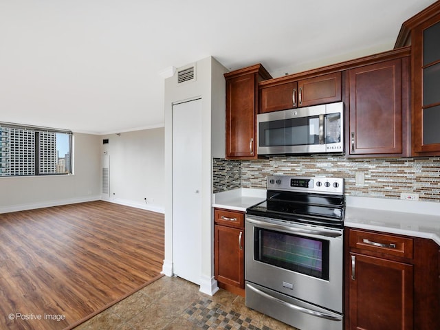 kitchen featuring appliances with stainless steel finishes, light countertops, baseboards, decorative backsplash, and ornamental molding
