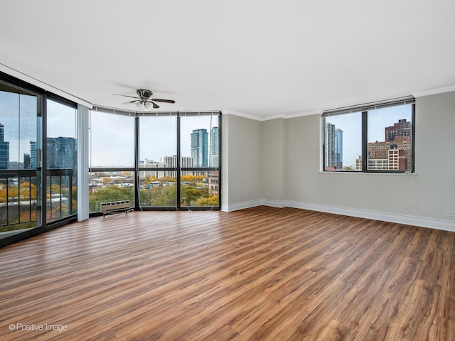 unfurnished room with a skyline view, wood finished floors, a ceiling fan, ornamental molding, and expansive windows