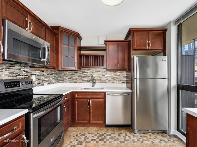 kitchen with appliances with stainless steel finishes, a sink, decorative backsplash, light countertops, and glass insert cabinets
