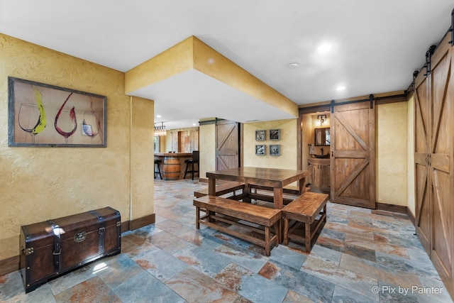 dining space featuring a textured wall, a barn door, stone tile flooring, and baseboards