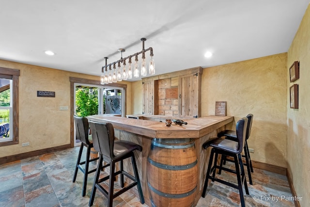 bar featuring a wealth of natural light, stone tile flooring, baseboards, and bar area