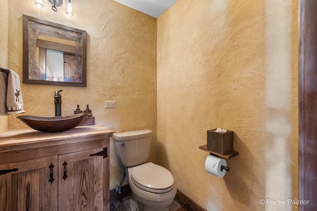 half bathroom featuring a textured wall, vanity, and toilet