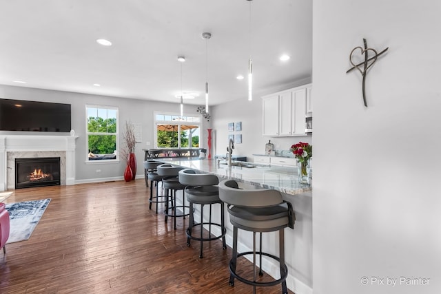 kitchen with light stone counters, a kitchen bar, dark wood-type flooring, white cabinets, and baseboards