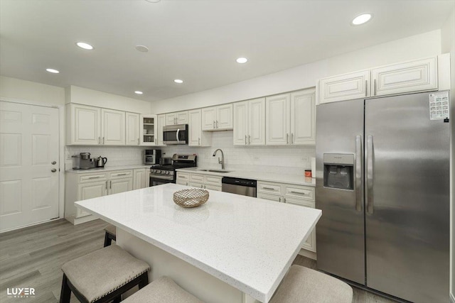 kitchen featuring a breakfast bar, stainless steel appliances, tasteful backsplash, light wood-style floors, and a sink