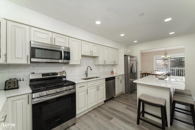 kitchen with appliances with stainless steel finishes, a sink, light wood-type flooring, a kitchen bar, and backsplash