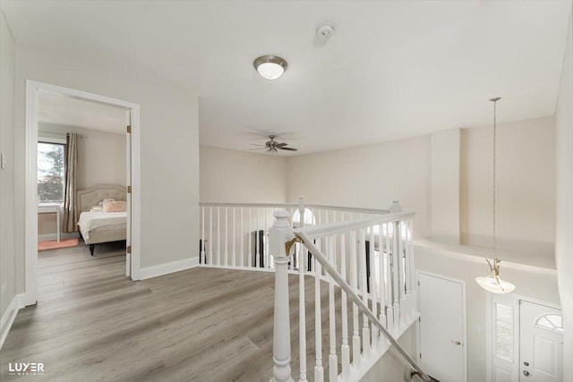 hall with wood finished floors, an upstairs landing, and baseboards