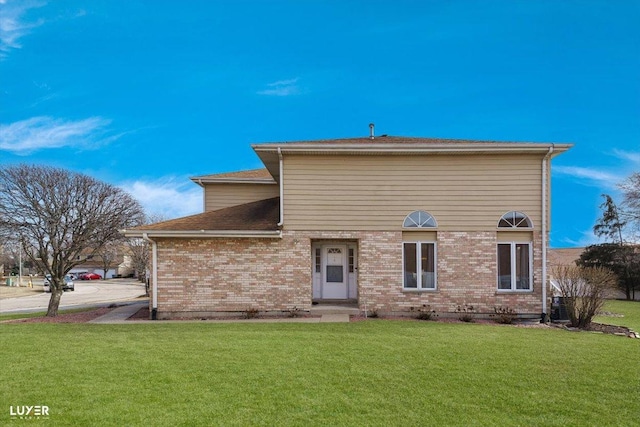 back of house featuring brick siding and a yard