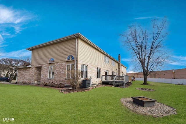 back of property with a deck, an outdoor fire pit, central air condition unit, fence, and a yard