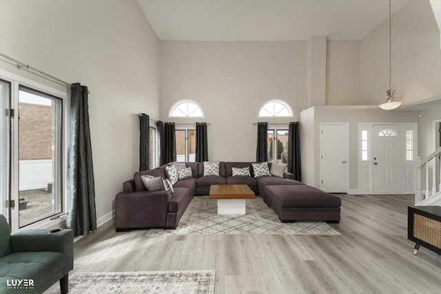 living area featuring a towering ceiling, plenty of natural light, light wood-style flooring, and baseboards