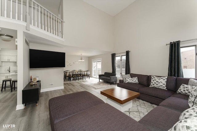 living room featuring baseboards, a high ceiling, a chandelier, and wood finished floors