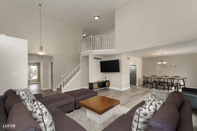 living room with visible vents, light wood-style flooring, high vaulted ceiling, baseboards, and stairs