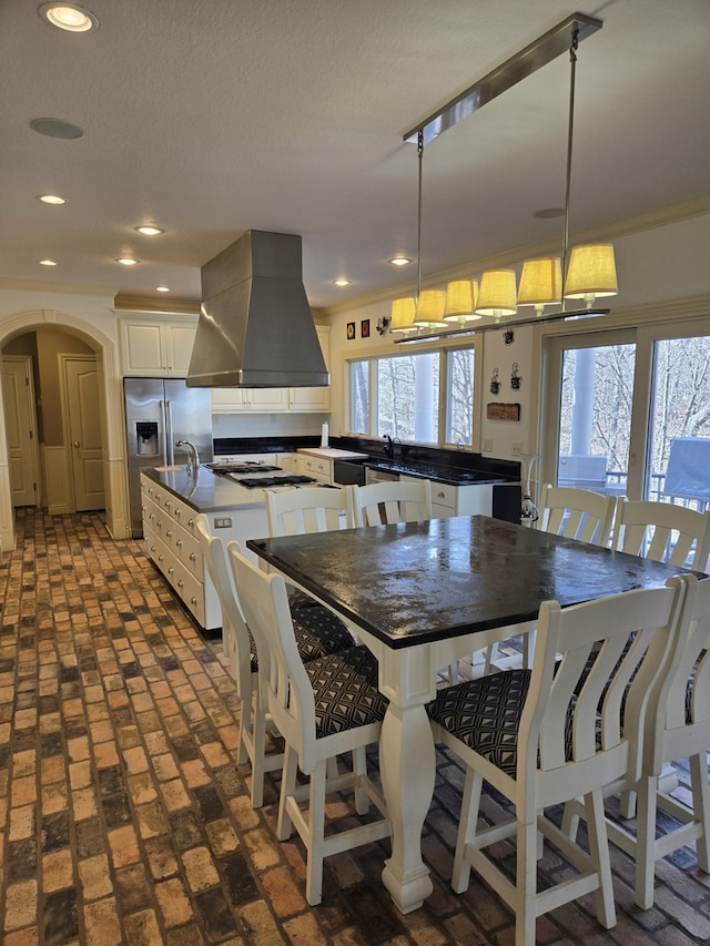 kitchen with arched walkways, dark countertops, a large island with sink, and island range hood