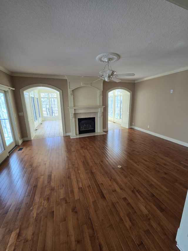 unfurnished living room with plenty of natural light, ceiling fan, dark wood-style flooring, and a fireplace with flush hearth