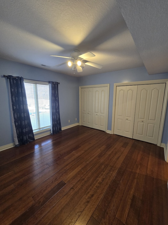 unfurnished bedroom with dark wood-style floors, baseboards, ceiling fan, and multiple closets