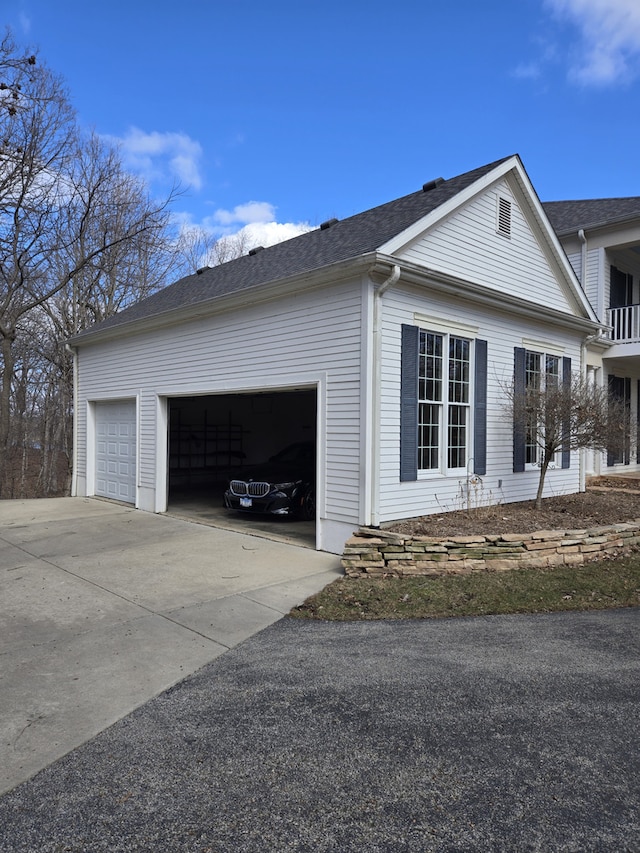 view of side of property featuring a garage, concrete driveway, and a shingled roof