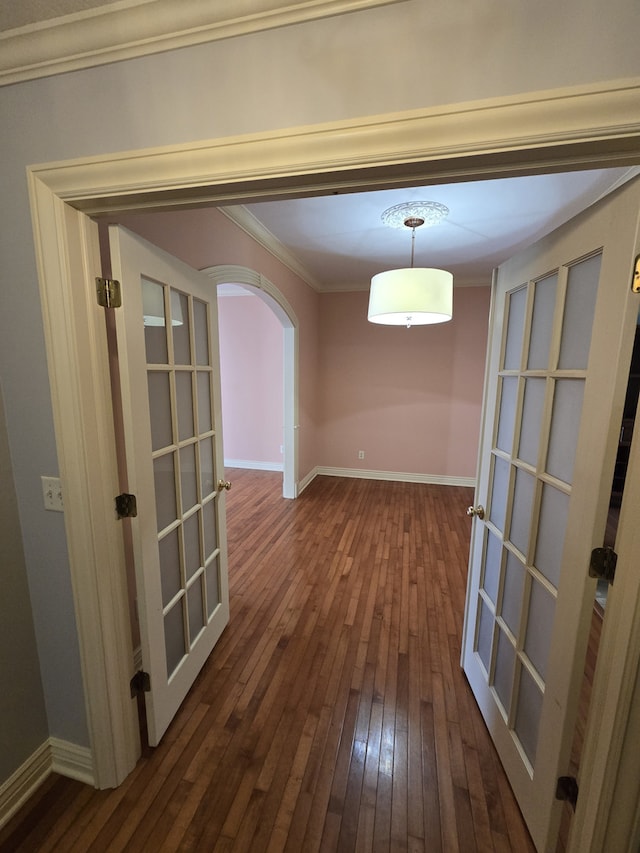 unfurnished dining area featuring arched walkways, baseboards, french doors, wood-type flooring, and crown molding