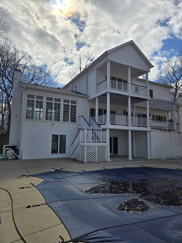 back of property with a balcony, stairs, a chimney, and a patio