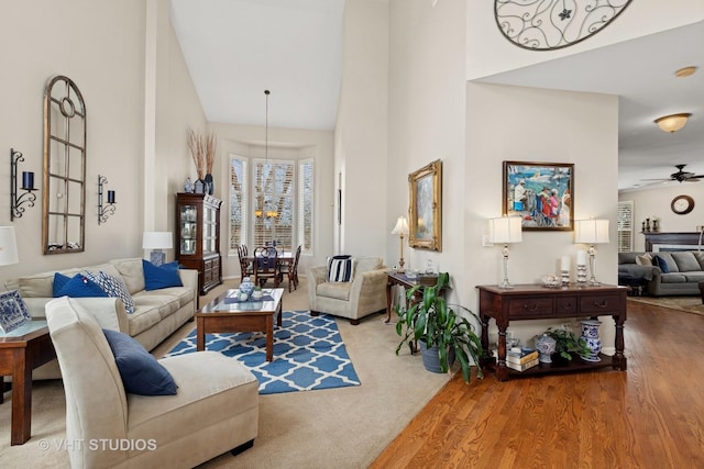 living room featuring a towering ceiling, wood finished floors, and ceiling fan with notable chandelier