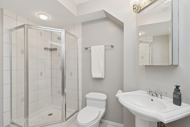 bathroom with toilet, a stall shower, baseboards, and a sink