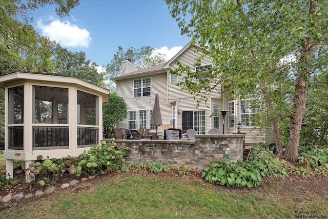 rear view of house with a sunroom, a chimney, and a patio