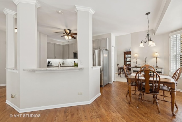 dining room with ceiling fan with notable chandelier, baseboards, wood finished floors, and ornate columns