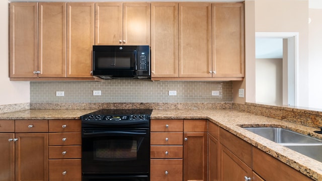 kitchen featuring light stone counters, a sink, decorative backsplash, brown cabinets, and black appliances