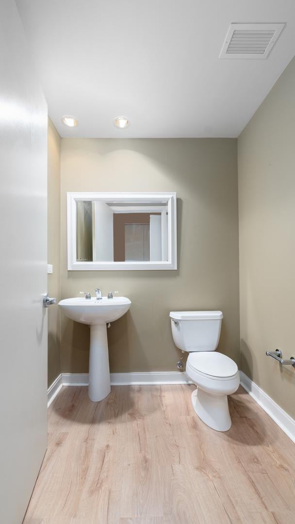 half bath with toilet, wood finished floors, visible vents, and baseboards