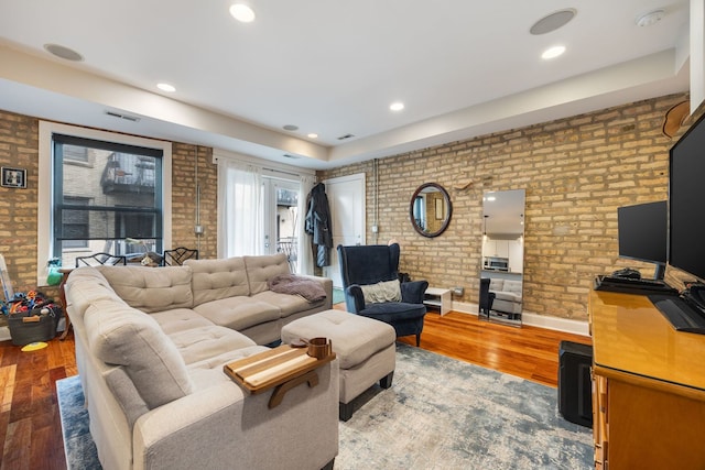 living room with recessed lighting, visible vents, brick wall, and wood finished floors