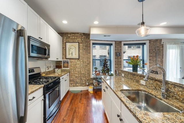 kitchen featuring white cabinets, dark wood finished floors, brick wall, stainless steel appliances, and a sink