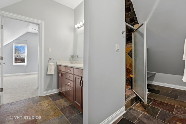 bathroom with vaulted ceiling, stone tile floors, baseboards, and a tile shower