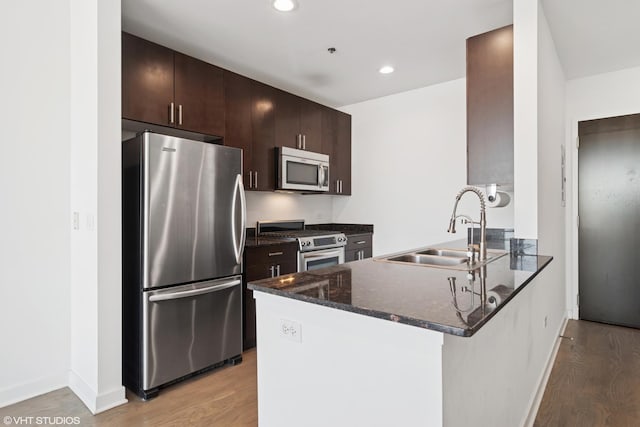 kitchen featuring dark brown cabinetry, appliances with stainless steel finishes, a peninsula, light wood-style floors, and a sink