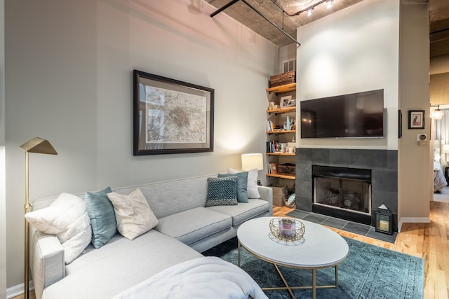 living room with a tile fireplace, wood finished floors, visible vents, baseboards, and track lighting