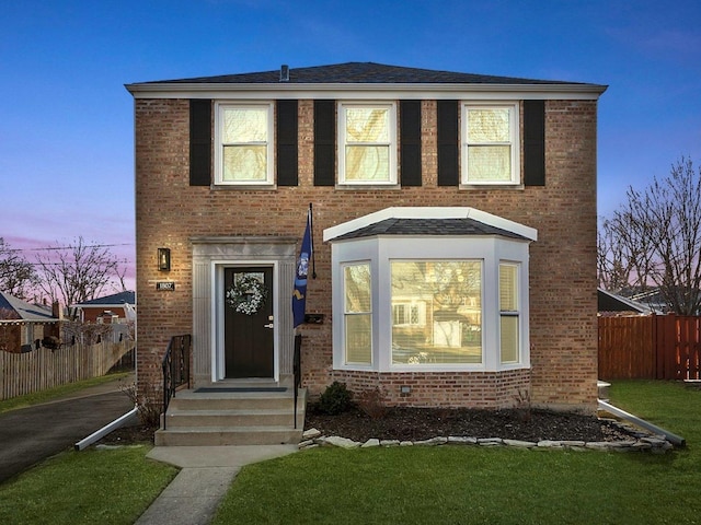 view of front of home with a yard, fence, and brick siding