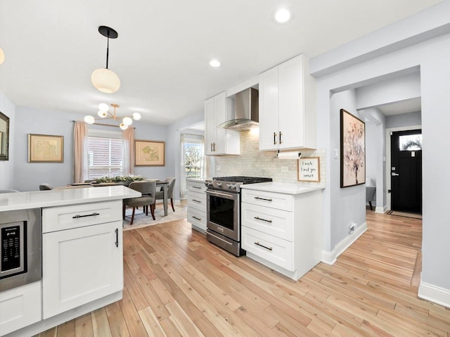 kitchen with light wood-style flooring, wall chimney range hood, backsplash, stainless steel appliances, and light countertops