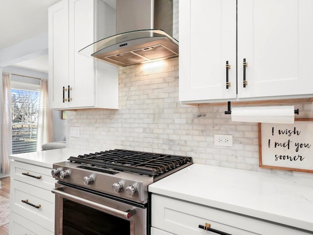 kitchen featuring stainless steel gas range oven, backsplash, wall chimney range hood, light countertops, and white cabinets