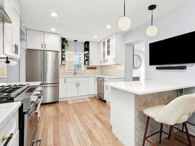 kitchen with open shelves, a sink, a kitchen breakfast bar, light countertops, and high end appliances