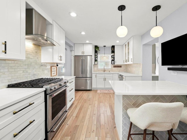 kitchen featuring a sink, decorative light fixtures, white cabinetry, stainless steel appliances, and wall chimney exhaust hood