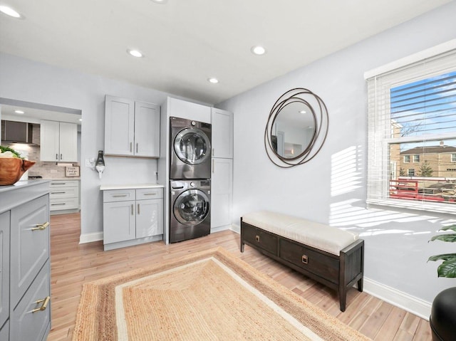 laundry room featuring light wood-style flooring, recessed lighting, baseboards, and stacked washer / drying machine