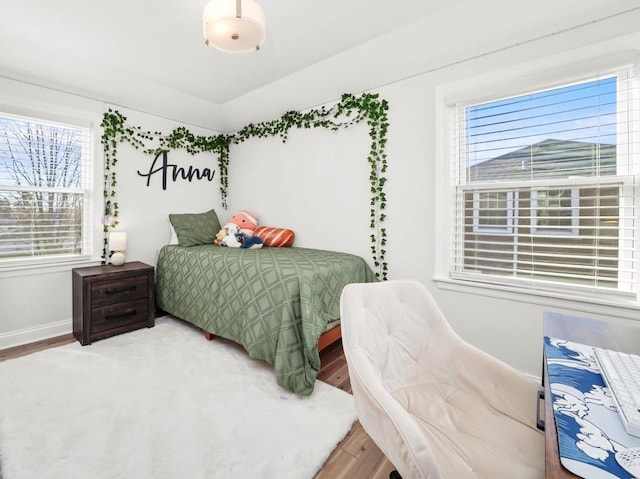 bedroom with multiple windows, wood finished floors, and baseboards