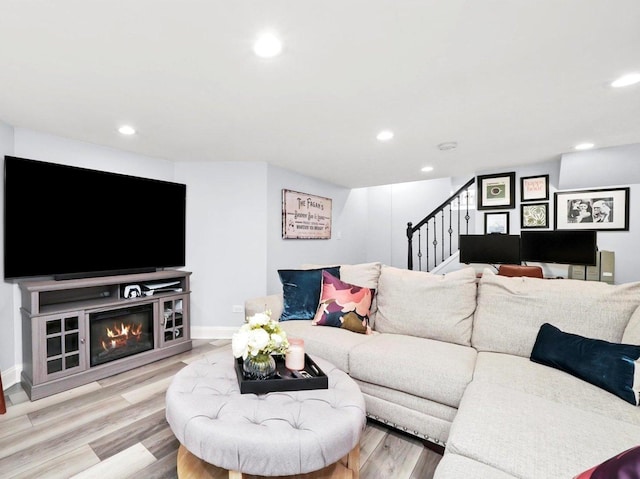 living area featuring baseboards, stairs, recessed lighting, light wood-style flooring, and a glass covered fireplace