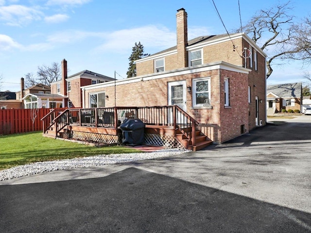 rear view of property featuring a lawn, fence, a wooden deck, brick siding, and a chimney