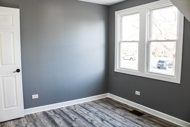 spare room with dark wood-type flooring, visible vents, and baseboards