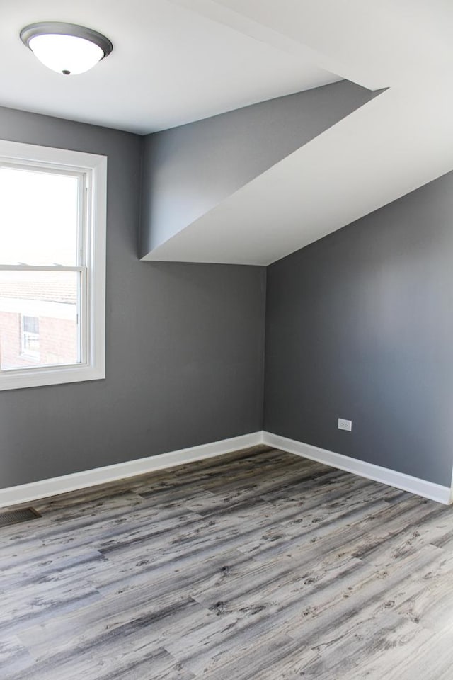 spare room featuring lofted ceiling, wood finished floors, visible vents, and baseboards